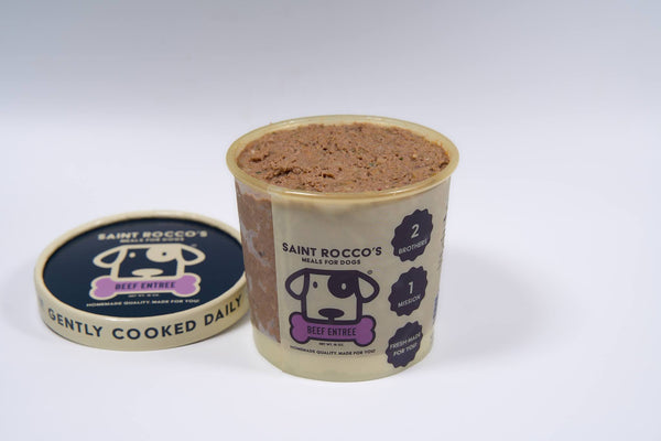 An open container of Saint Rocco’s Beef Entree by Saint Rocco’s Treats reveals the dog food inside, while the lid with the brand's logo and text on a white background sits nearby.