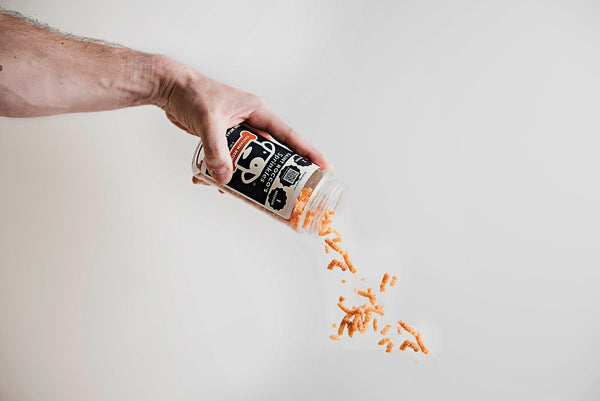 A hand holding a bottle of 'Chicken Sprinkles' with orange-colored sprinkles pouring out of the bottle onto a surface.