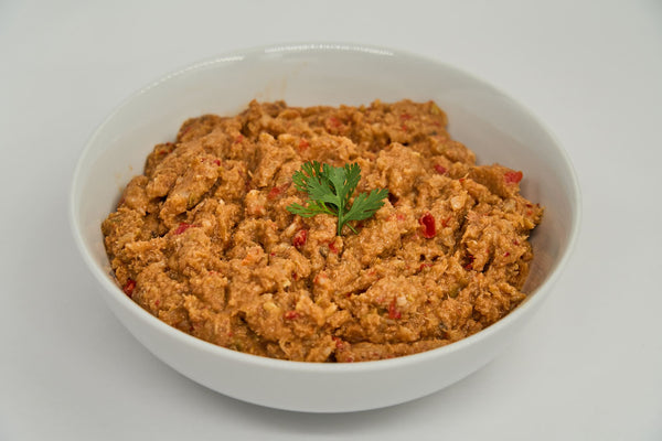 A white bowl holds Saint Rocco's Cod & Salmon Entree by Saint Rocco's Treats, a creamy reddish-brown dog food garnished with fresh cilantro, set against a plain white background.