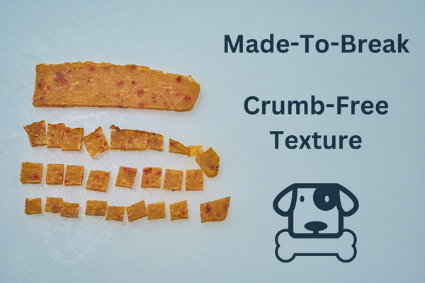 A rectangular Saint Rocco's Treats Chicken and Sweets artisan dog treat is broken into small squares. Text reads Made-To-Break, Crumb-Free Texture with a cartoon dog chewing a bone icon. Plain white background. Ideal for training rewards!.