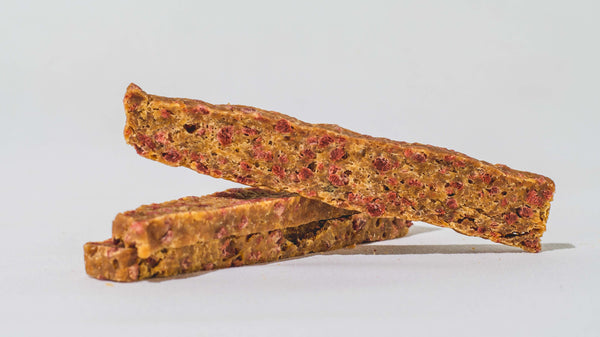 Two rectangular granola bars with visible red fruit pieces are stacked on a white surface with a plain white background.
