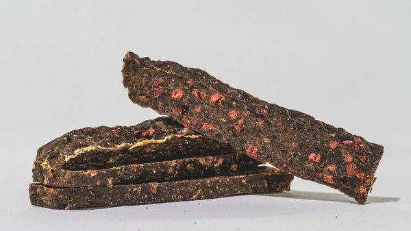 Three dark brown bars with red specks are stacked on a light surface; one is angled on top, showcasing Saint Rocco's Treats' Specialty Bundle as the ideal high-value dog treat for training or rewarding your pup.