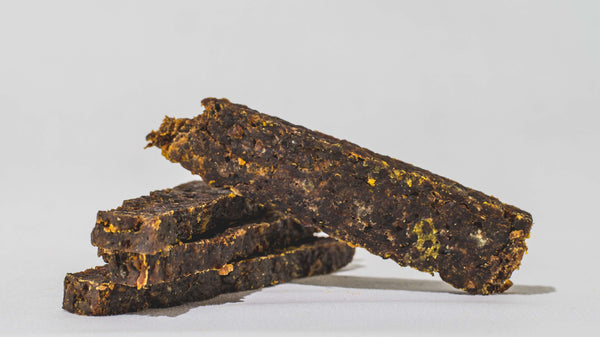 Four pieces of Saint Rocco's Treats Specialty Bundle are stacked on a plain white background, showcasing their dark brown, dry, textured surfaces with visible bits of seasoning.