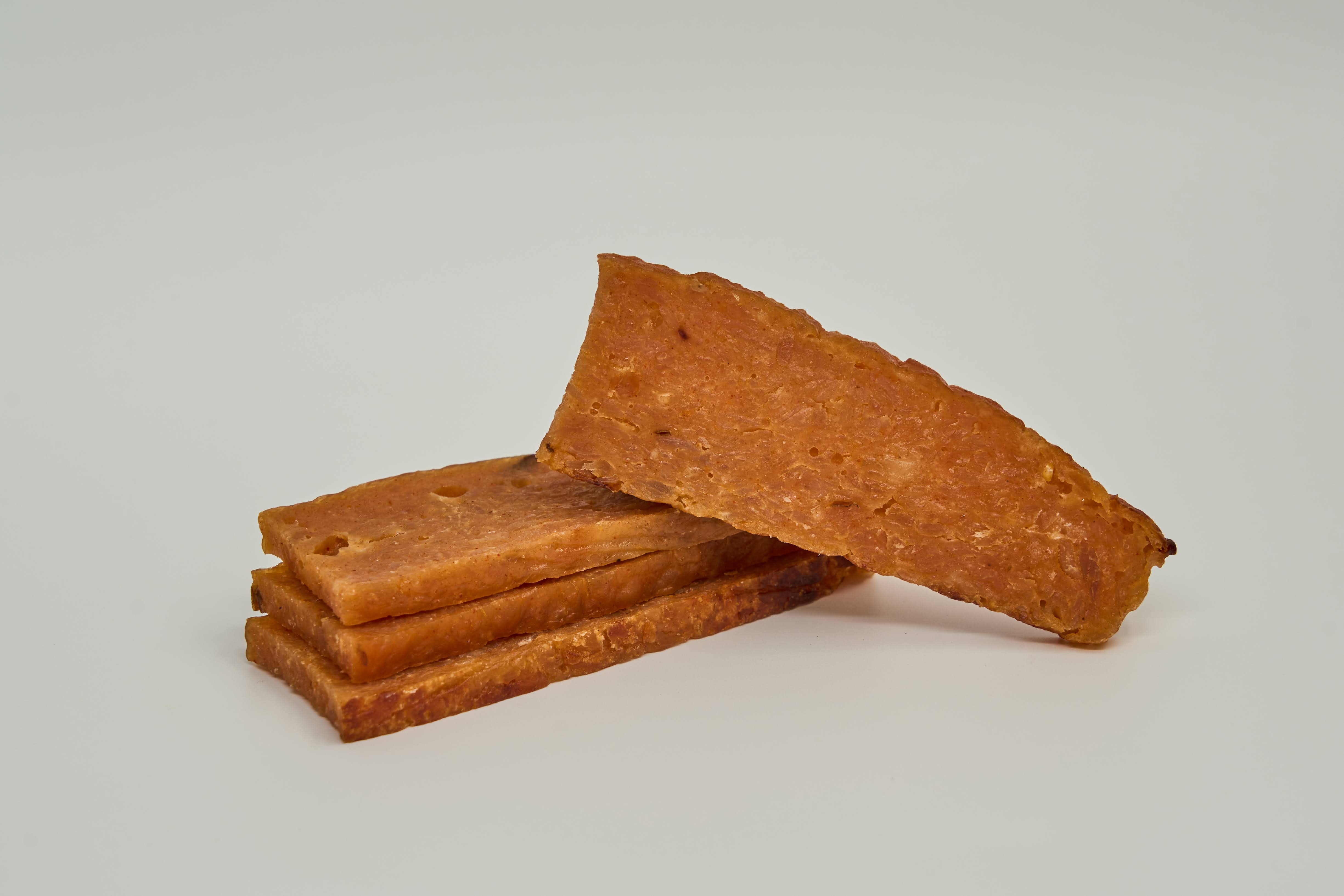 Rectangular, crispy baked Chicken and Honey Treats from Saint Rocco's Treats are stacked, with one leaning against the pile, displayed on a plain light background.