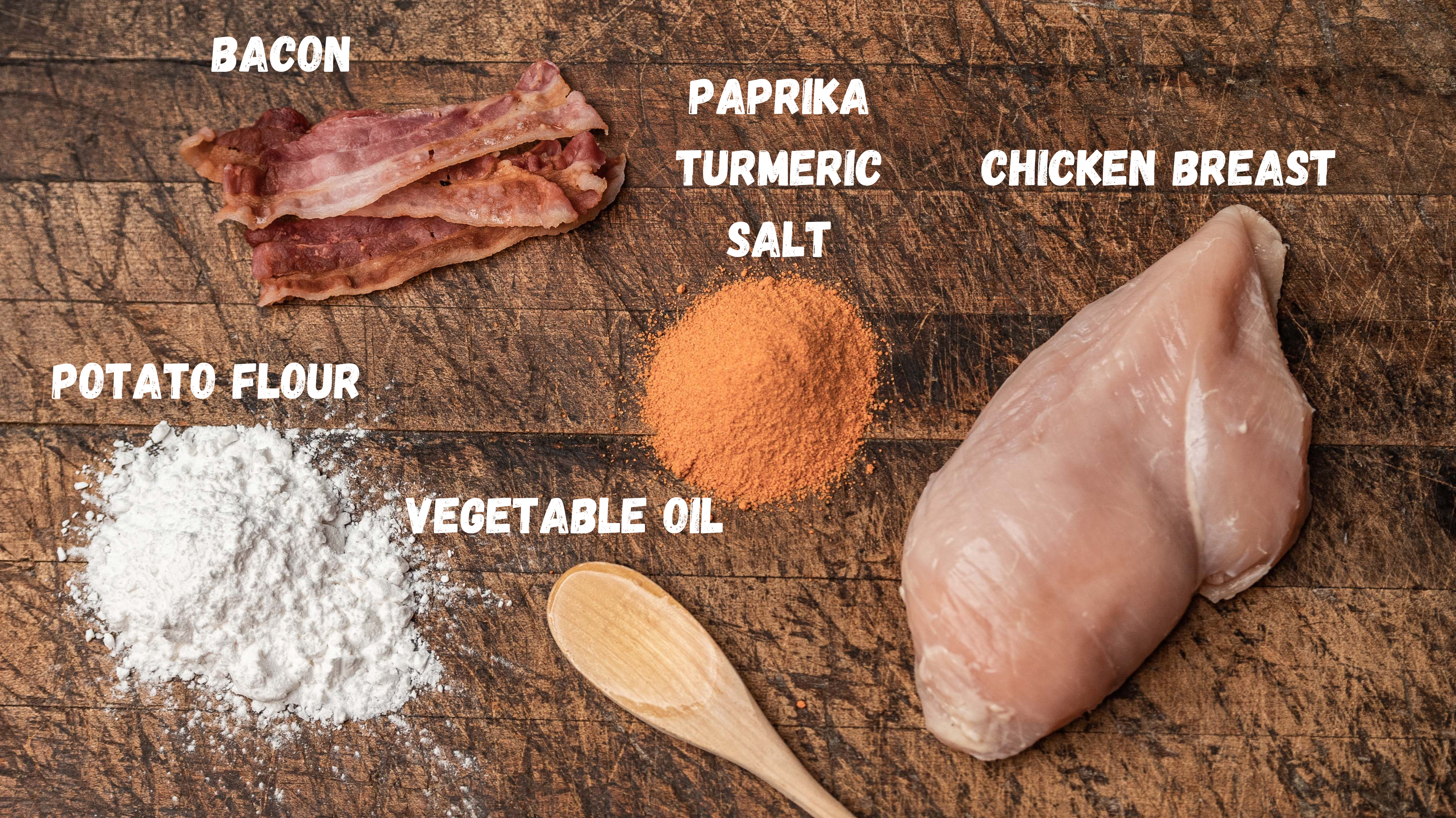 A wooden surface shows raw chicken breast, bacon strips, potato flour, paprika, turmeric, salt, and vegetable oil—key ingredients in Saint Rocco’s Treats Meat Lover Treats. Each ingredient is labeled for this artisan dog treat recipe.