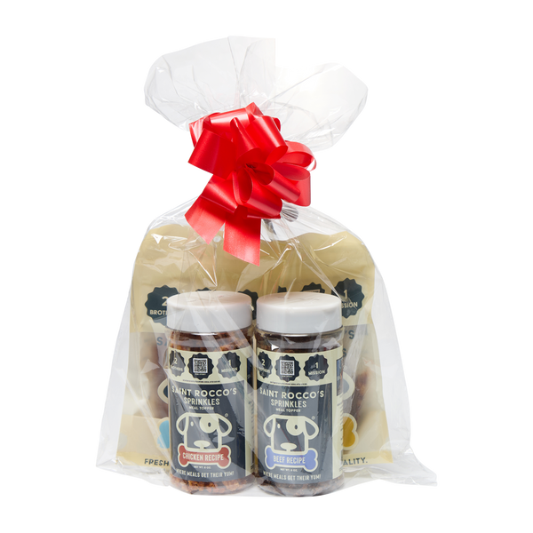 The Saint Rocco's Sprinkles Stocking Stuffer by Saint Rocco's Treats features two bottles of dog sprinkles (chicken and beef) and two pouches of broth powder in a clear gift bag with a red bow, perfect for pets and shown on a white background.