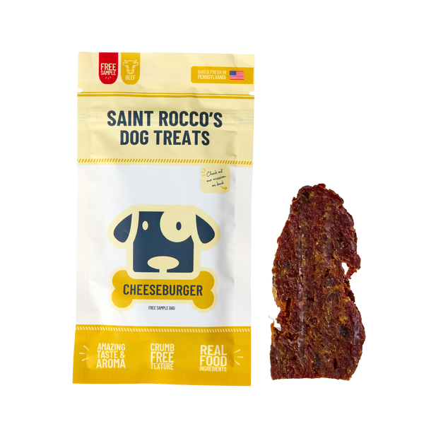 A bag of Saint Rocco's Treats Sample Treat with a cartoon dog on the packaging is shown next to a single, brown, irregularly-shaped treat on a white background—perfect for pups who love meat treats.